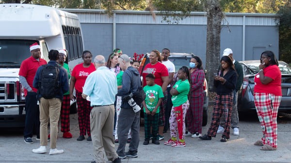 A diverse group of people in festive attire gathers outside, chatting and enjoying the holiday atmosphere, likely participating in a community event.