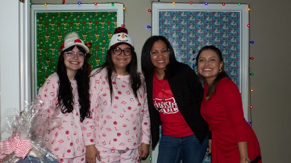 Four women pose together in festive attire, smiling in front of colorful, decorated backgrounds.